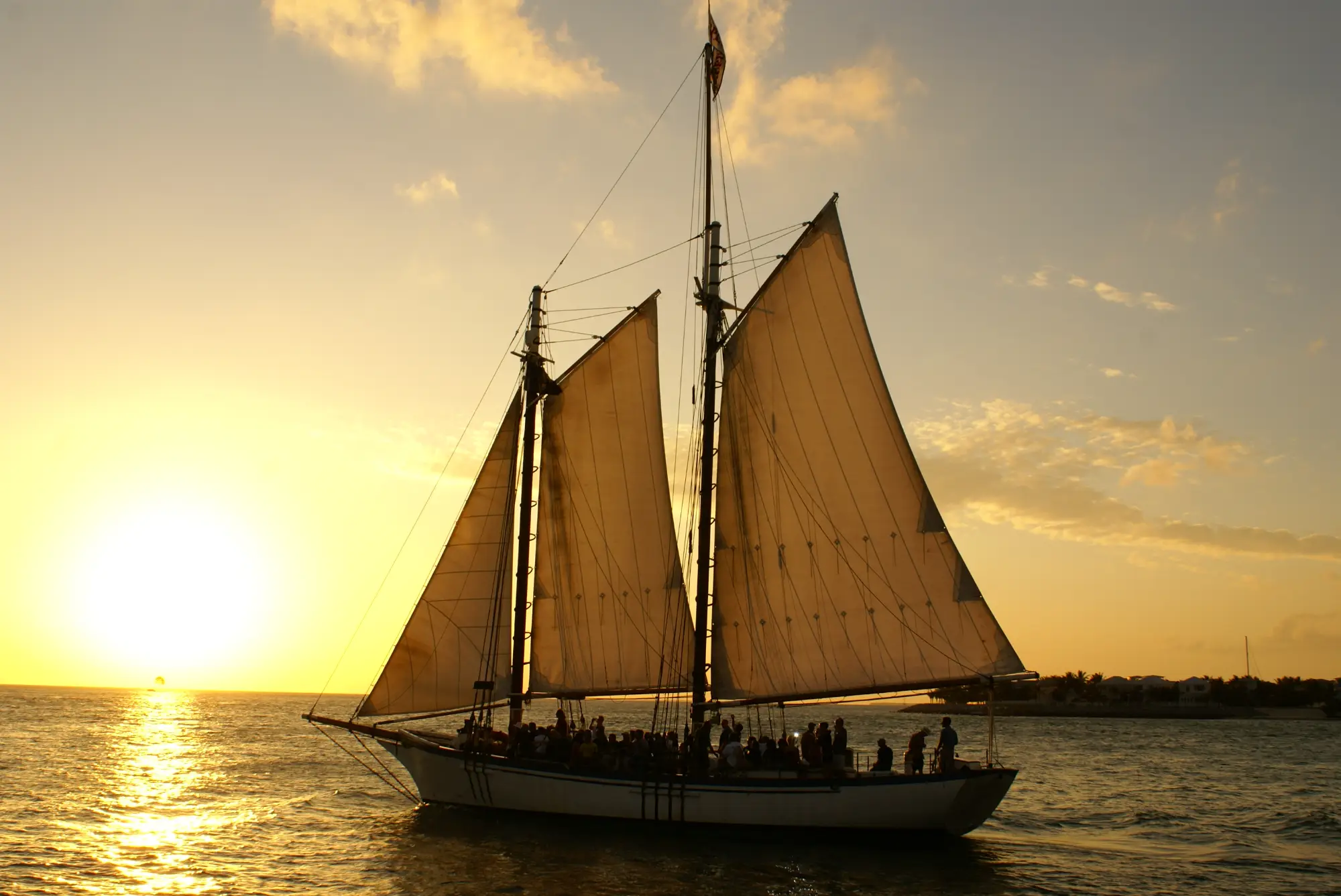 Two-masted schooner with passengers sailing past the setting sun off Key West