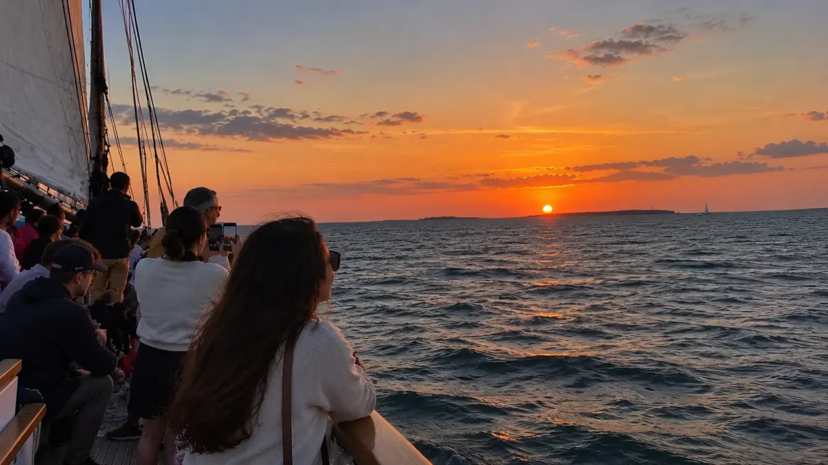 Guests watching an orange sunset from the deck of the schooner