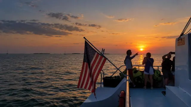 Guests at the stern with an American flag watching the sun set over the water