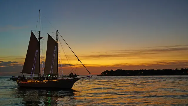 Schooner strung with lights carrying passengers past Mallory Square at sunset